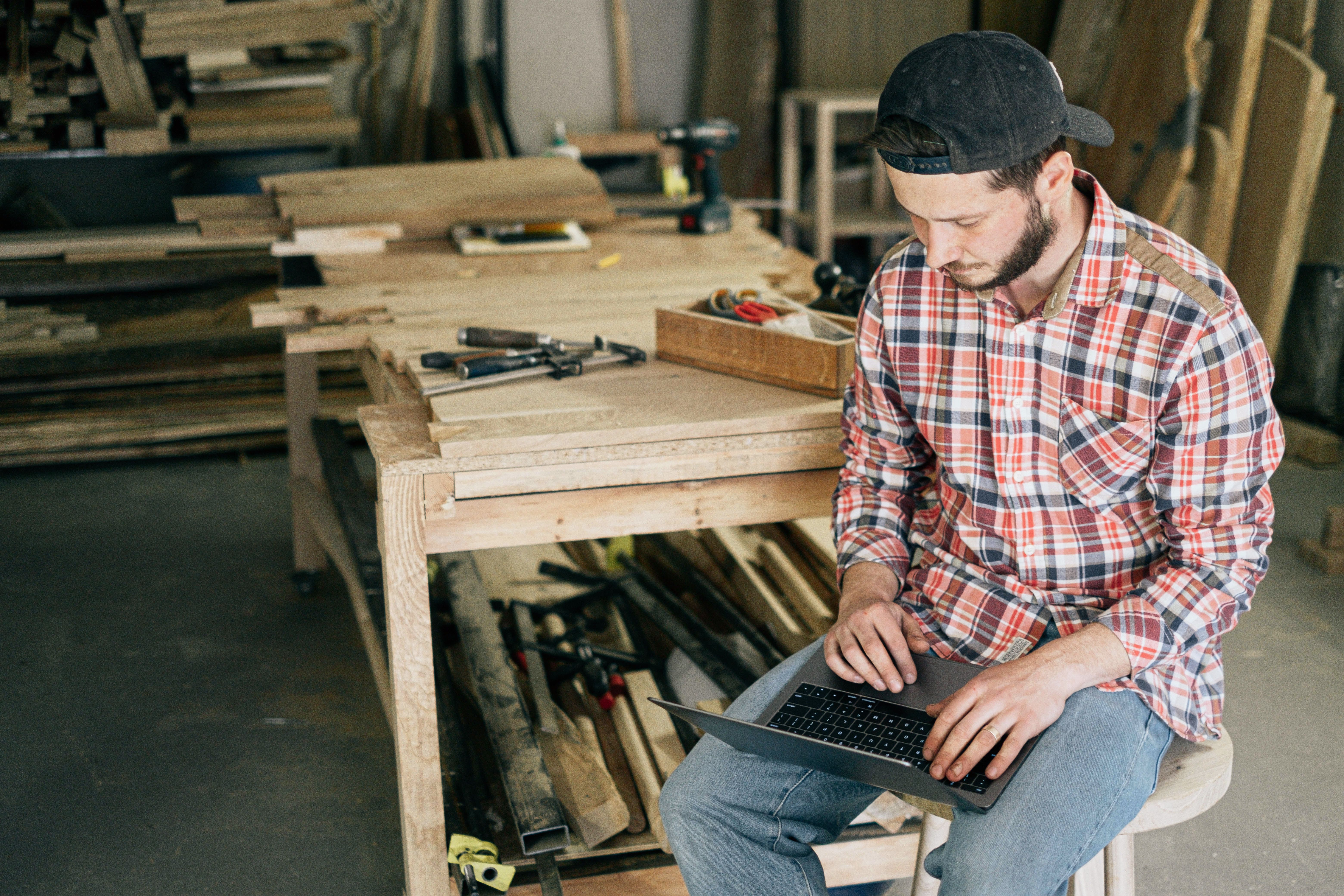 Carpenter in a plaid shirt checking a tablet at his workshop bench